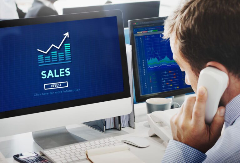 A salesperson is on a call while a monitor screen displays an increasing sales graph.